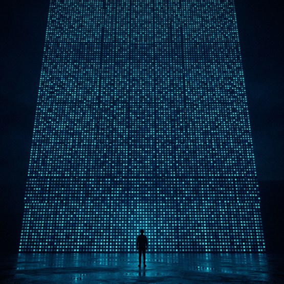 A lone figure standing at the foot of an immense wall of tiny lit panels that runs off the top of the frame